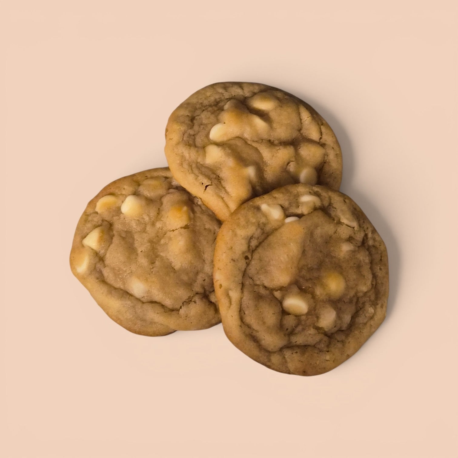 Three golden-brown chocolate chip cookies with white chocolate chips, arranged in a small pile on a solid light beige background.